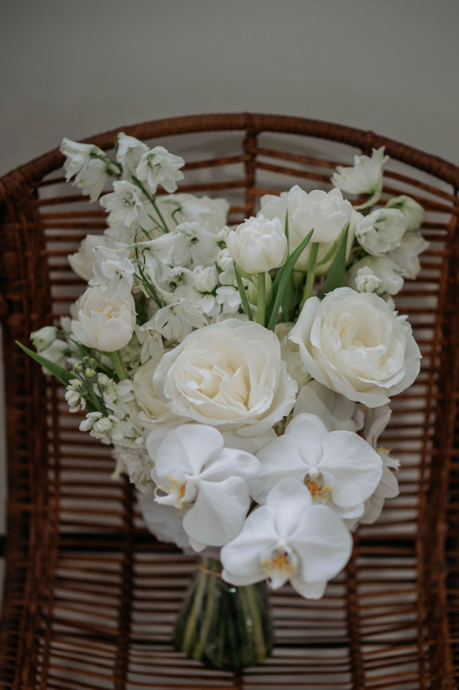 White wedding centerpiece featuring elegant roses and orchids arranged in a decorative display against a woven backdrop.