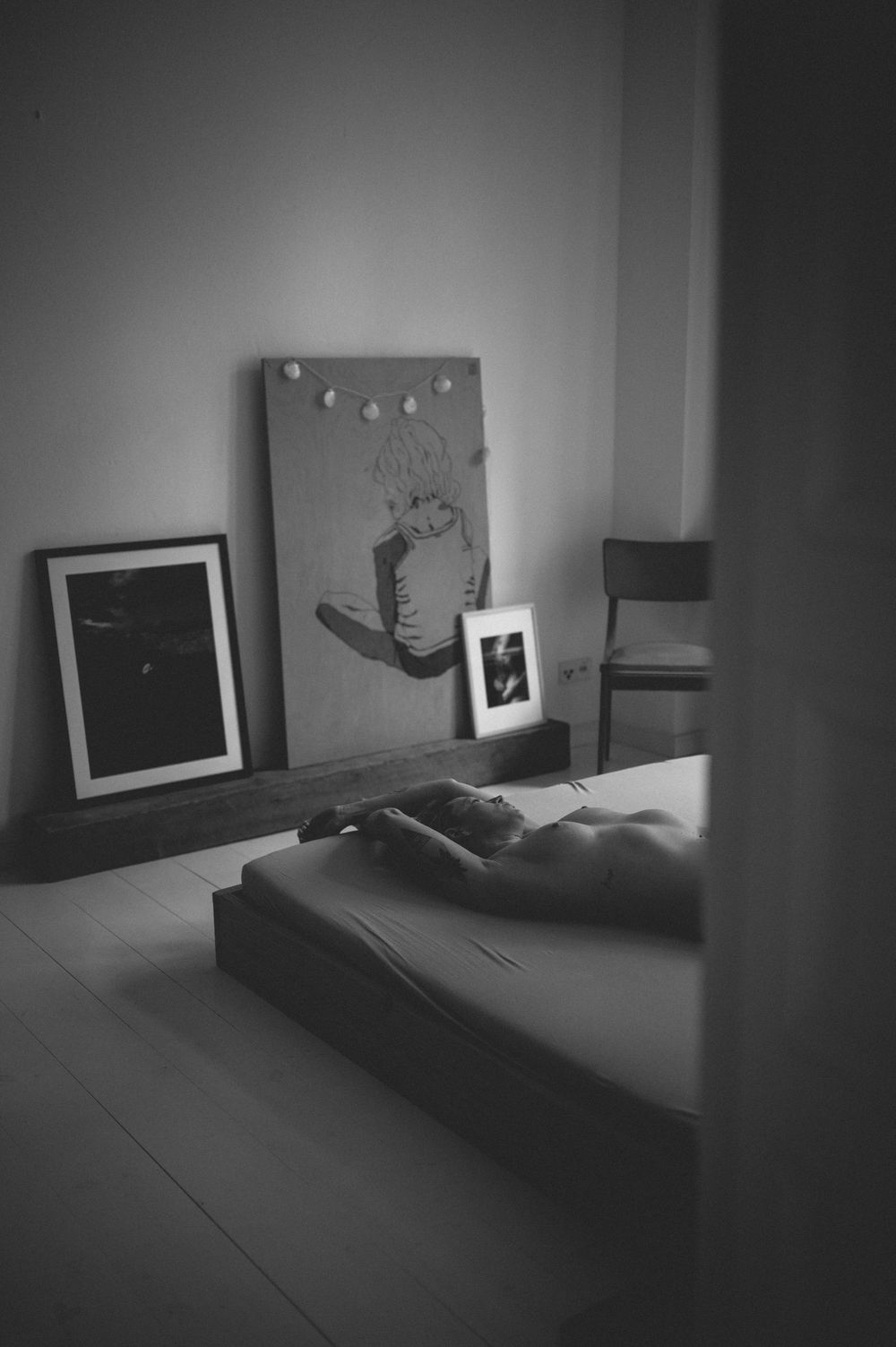 A minimalist bedroom with monochrome artwork on wall and mattress on floor in black and white photography.