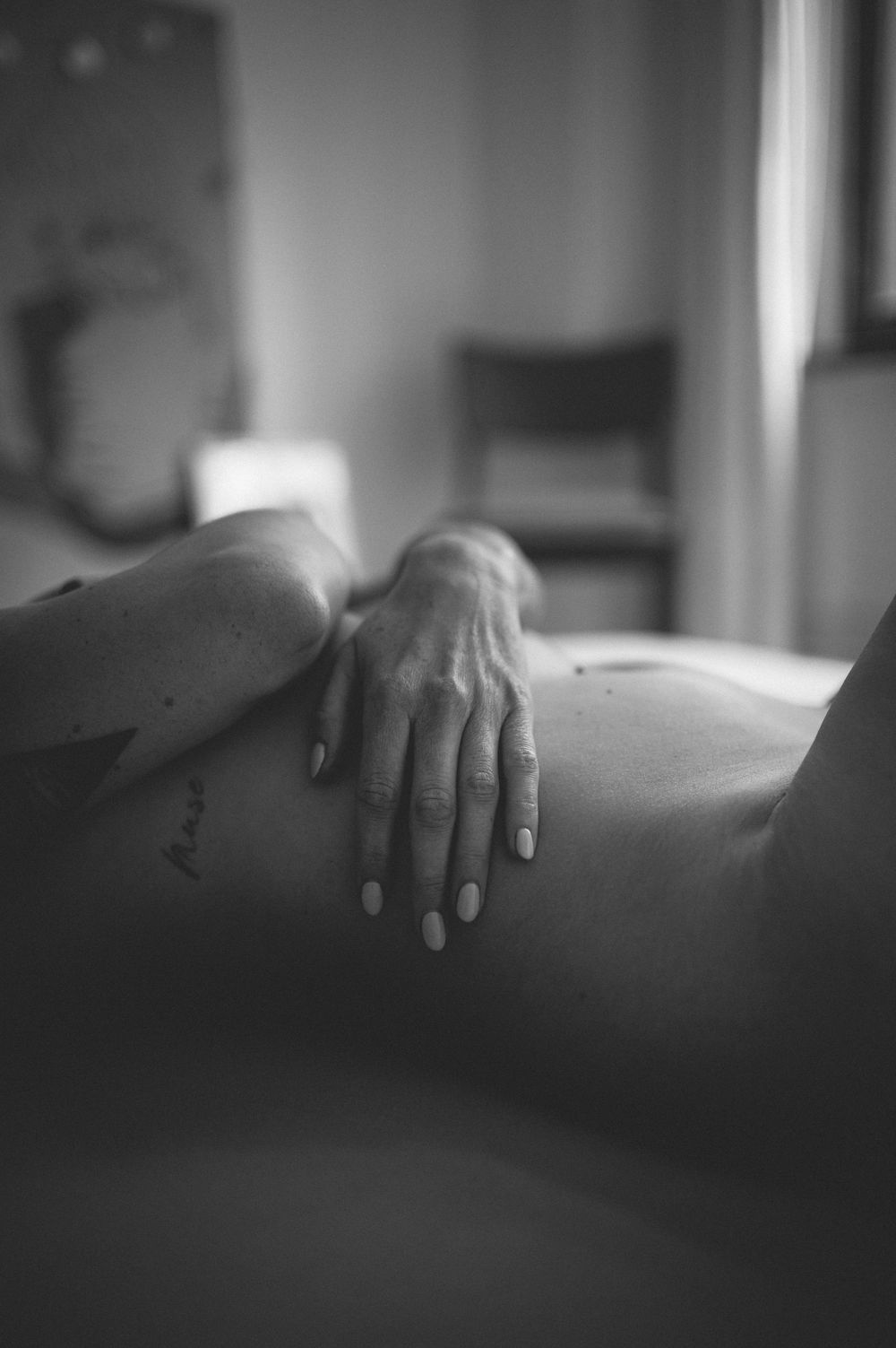 A black and white artistic photo showing a hand resting on bare skin in soft, intimate lighting.