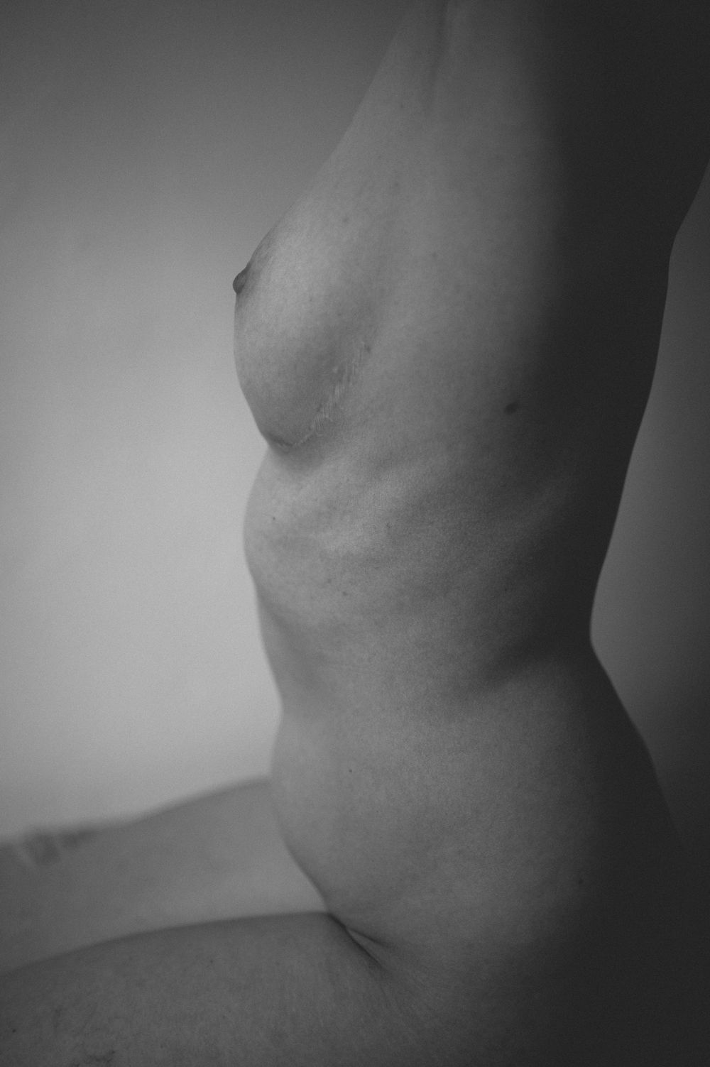 Black and white artistic nude photograph showing abstract curves and shadows of a torso form.
