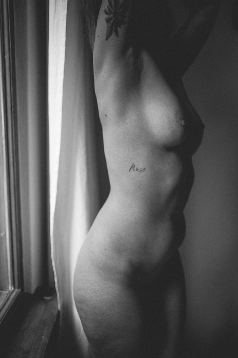 Artistic black and white photo of a nude torso silhouetted against window light in a minimalist style.