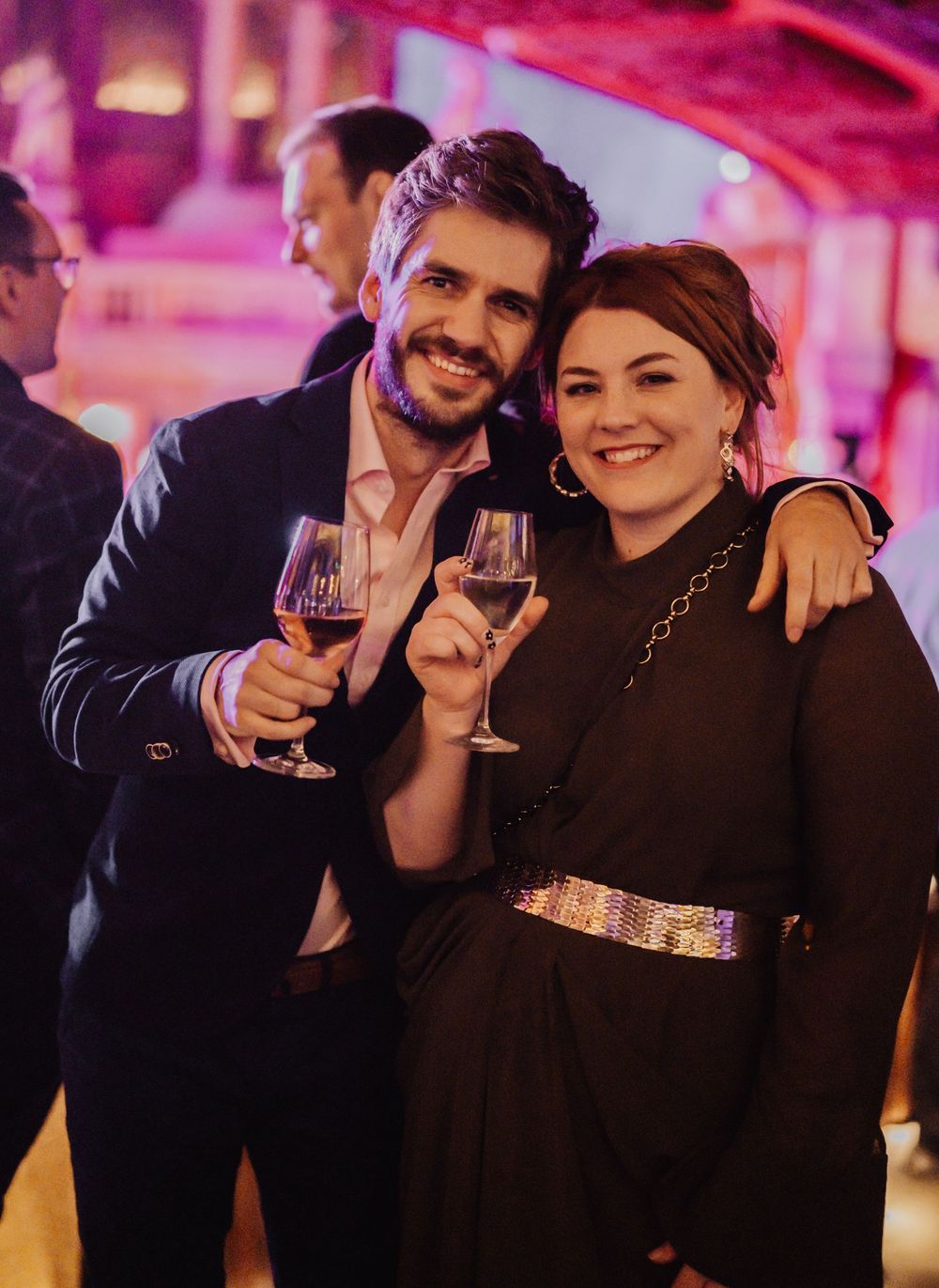 Couples enjoying drinks and conversation in a dimly lit venue with pink ambient lighting.