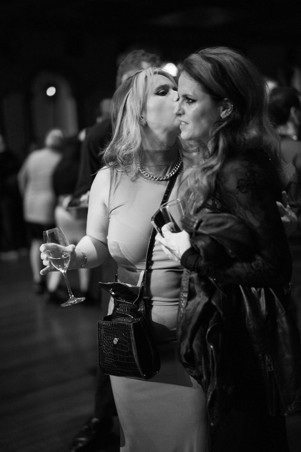 Artistic black and white photo of party guests mingling with wine glasses at a social gathering.