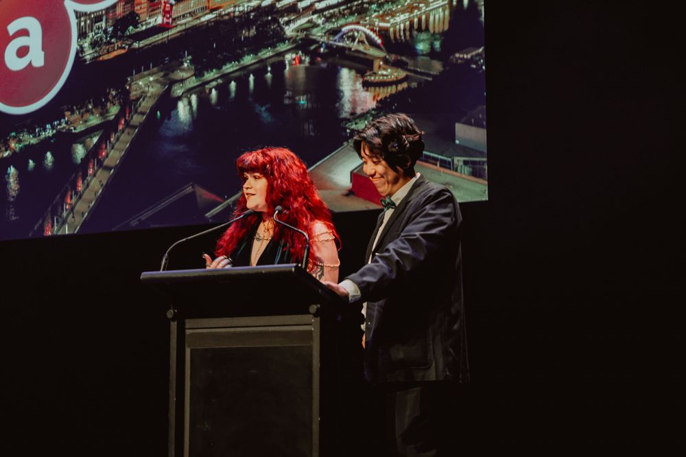 A person in red attire plays piano while another person in dark clothing stands beside them during a performance.