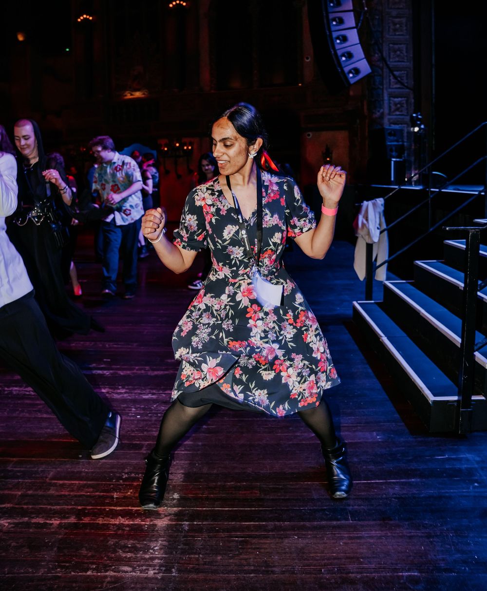 A person in a floral dress dances energetically on a dark stage, showing elegant dance moves at a nighttime venue.