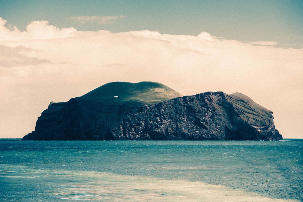 A panoramic series of misty ocean islands under a soft cloudy sky stretches across the horizon in blue tones.