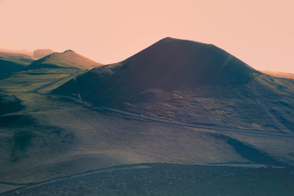Rolling green mountain peaks silhouetted against an orange-tinted sky during sunset.