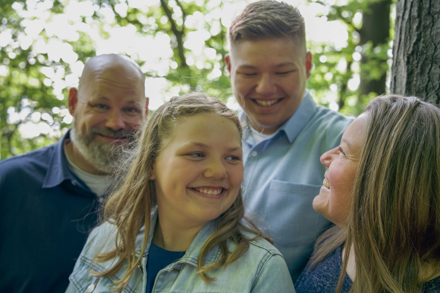 A group in casual attire poses together outdoors for a portrait among green trees on a sunny day.