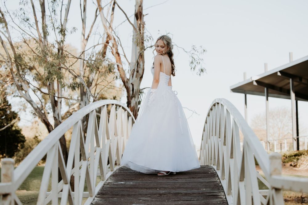 girl in white dress walks along a wooden boardwalk surrounded by eucalyptus trees at sunset.