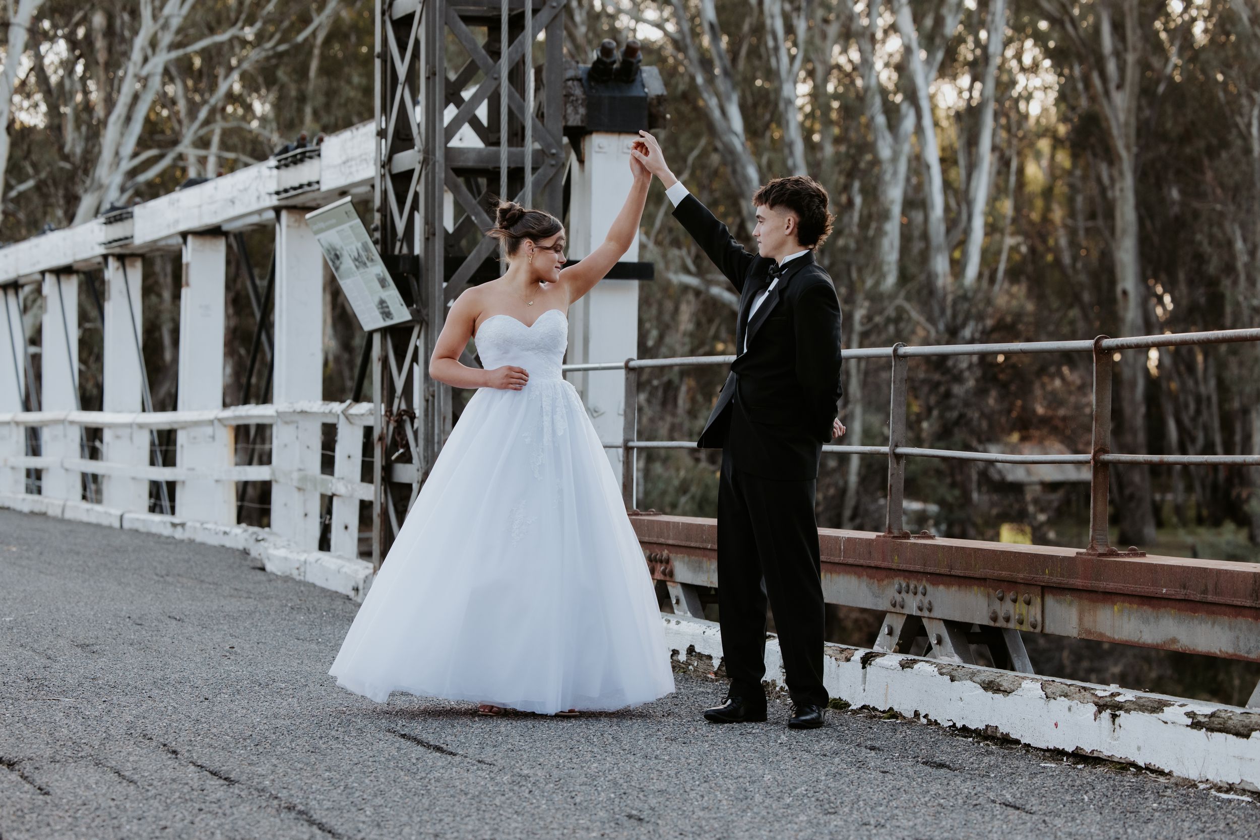 Deb couple walks hand in hand through a wooded area with white picket fences creating a romantic outdoor setting.