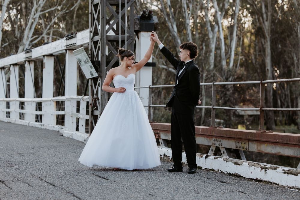 Deb couple walks hand in hand through a wooded area with white picket fences creating a romantic outdoor setting.