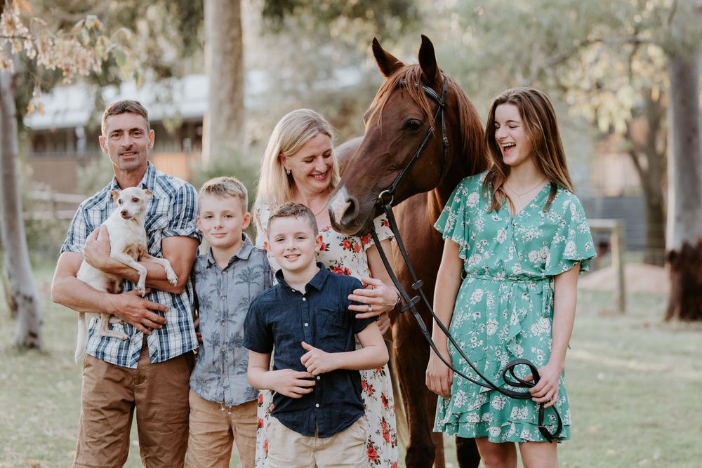 Family photo session outdoors with a brown horse in a grassy field at sunset.