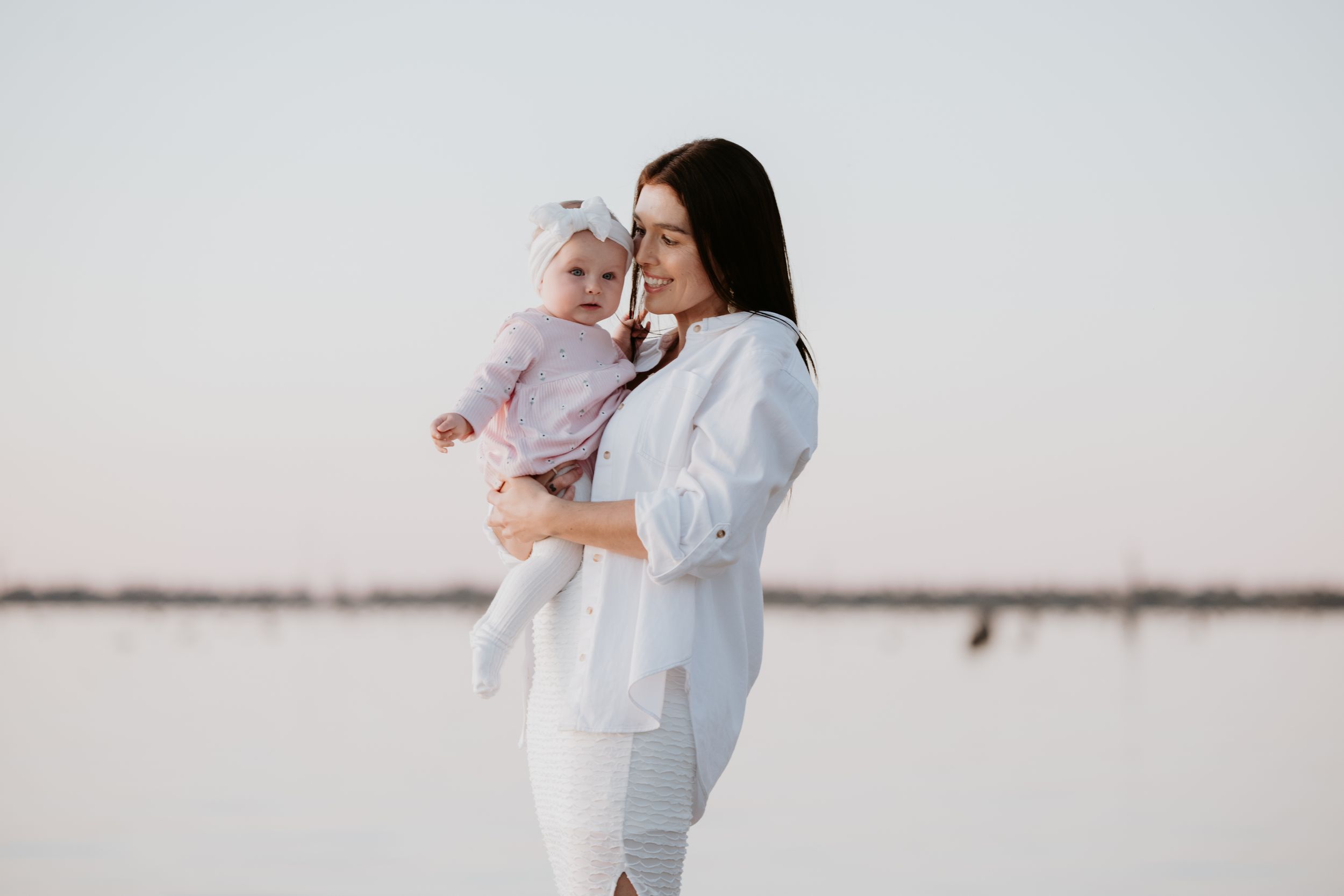 A parent in white holds a baby against a bright, minimalist background creating a tender family moment.