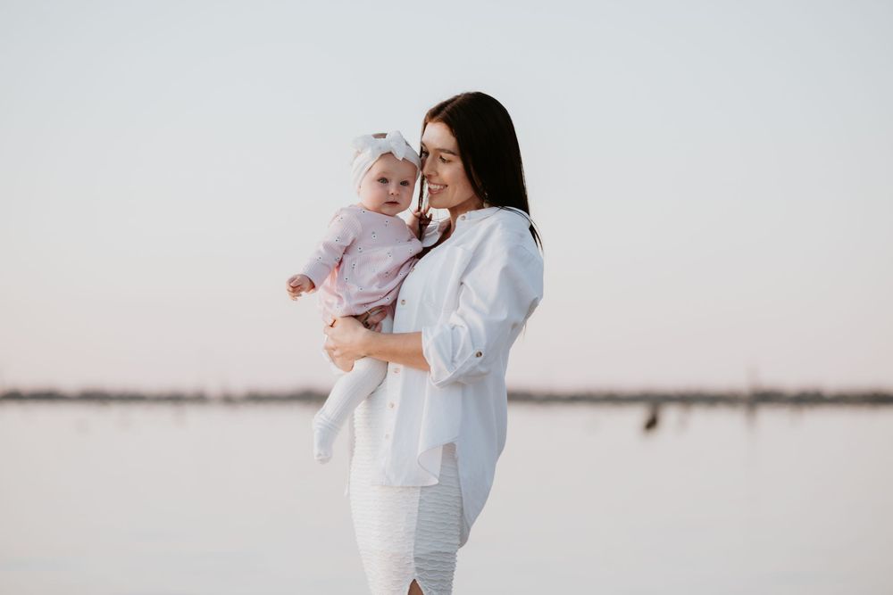 A parent in white holds a baby against a bright, minimalist background creating a tender family moment.