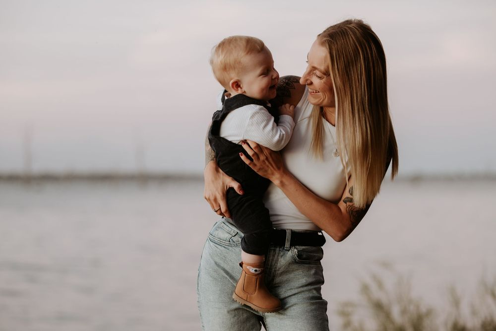 A series of intimate black and white photos showing tender moments between parent and child by the water at sunset.