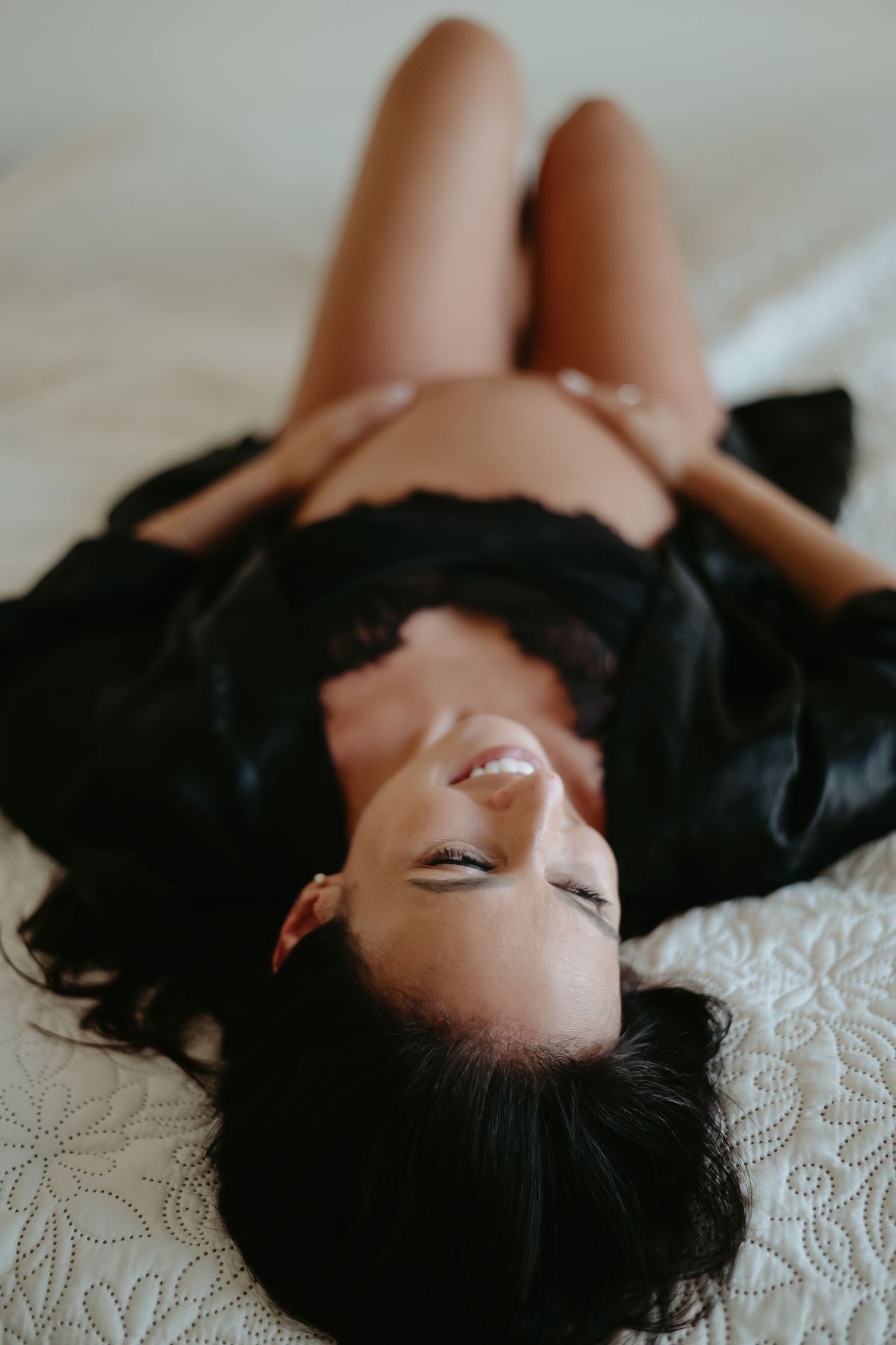 Intimate boudoir portrait of woman with dark hair lying on textured bedding.