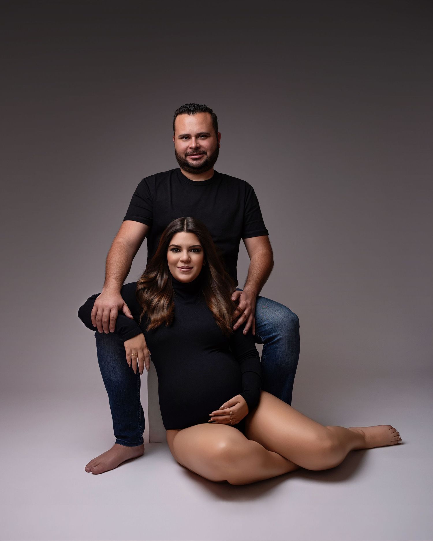 Elegant maternity portrait in studio setting with dramatic lighting and black attire.