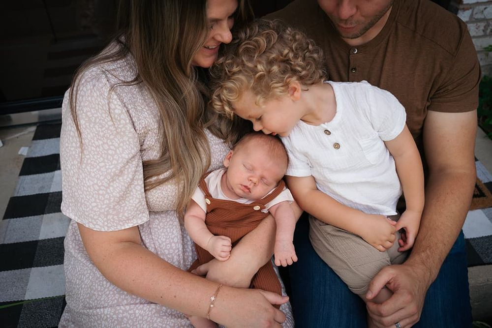 A family sits together on a black and white checkered floor, holding a sleeping newborn baby and toddler in Evanston, IL