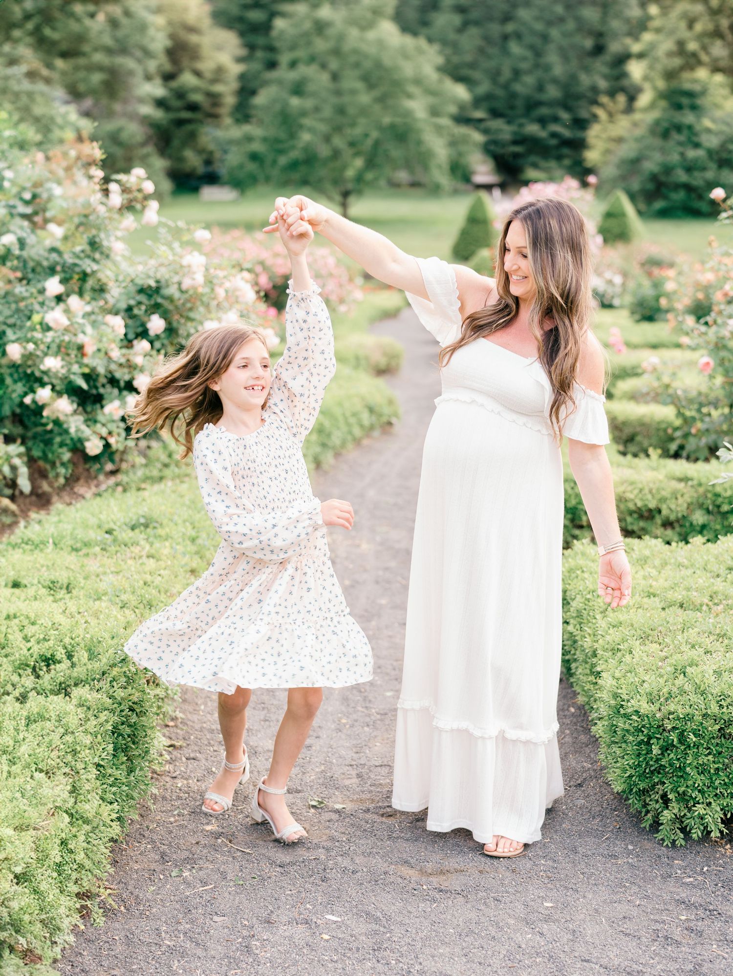 Joyful mother and daughter spinning and dancing in a garden of beautiful flowers at Deep Cut Gardens during a golden hour session.