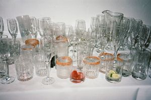 A collection of clear glass drinking vessels and cocktail glasses arranged on a white surface with citrus garnishes.