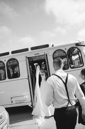 Group of people in light clothing boarding a vintage public transit bus in black and white photography.