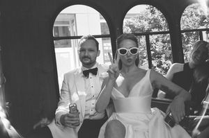 Black and white photo of a wedding celebration with guests in formal attire enjoying drinks outdoors on a sunny day.