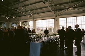 Silhouettes of people gathered at an indoor event space with large windows and a decorated table in soft natural lighting.