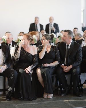 Formal event attendees in black attire seated in rows at an indoor venue.
