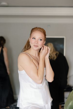 Bride in white silk getting ready in bridal suite with soft window light.