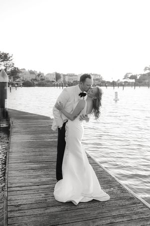 Romantic couple poses during sunset on wooden pier for wedding photos in black and white.