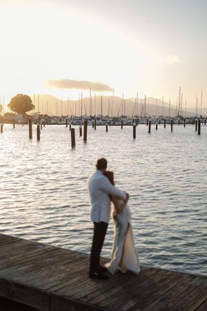 A couple embraces on a dock at sunset with boats and mountains in the background. Gallery 308 San Francisco Wedding Photographer