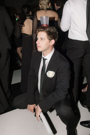 A person in formal attire sitting in a dimly lit room during an event.