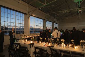 Elegant dinner reception setup with glowing candles and large windows overlooking a city skyline at dusk.