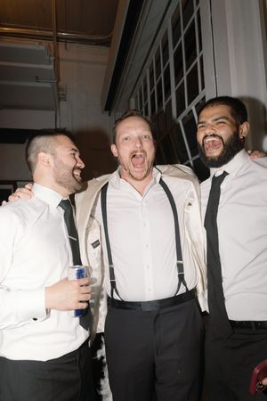 Groomsmen in white shirts and suspenders laughing and joking together at a wedding celebration.