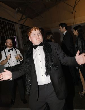 A person in formal attire dances energetically at an indoor event wearing a black suit jacket and white dress shirt.