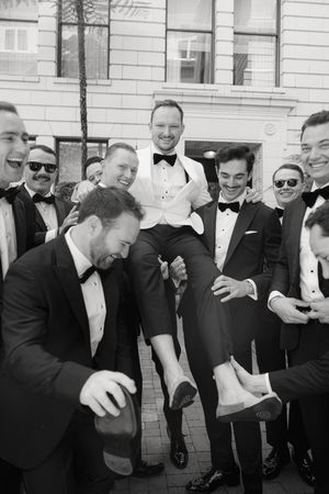 Group of groomsmen in tuxedos laughing and posing together in black and white.