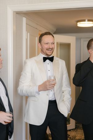 Group of men in formal attire enjoying drinks and laughs in a hotel room.