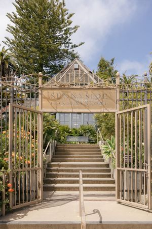 Ornate garden entrance with stone steps and metal gates leading to a conservatory.