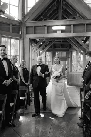 Individuals in formal attire stand together in an elegant indoor space with large windows and exposed beams.