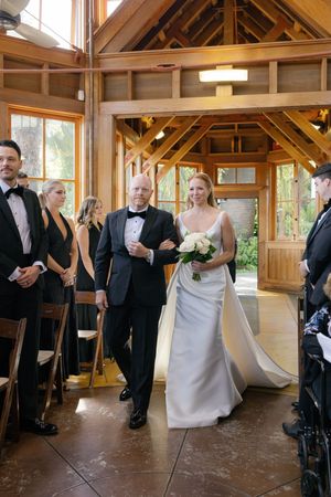 Wedding procession walking down the aisle in a rustic wooden chapel with warm lighting.
