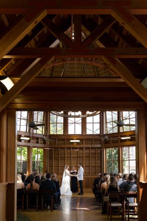 A rustic wooden ceremony hall with exposed beams and large windows during a daytime event. Sunnyside conservatory in San Francisco