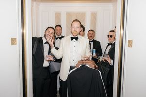 Groomsmen in formal attire sharing a candid moment in a doorway.