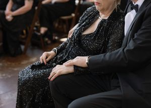 Close-up detail of formalwear showing a sparkly black dress and tuxedo at an elegant event.
