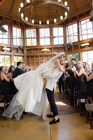 A newlywed couple performs a dramatic dip on the dance floor surrounded by guests in a circular venue.
