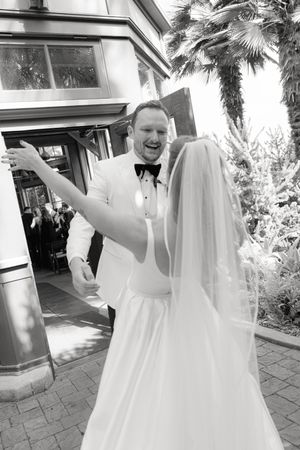 Black and white photo of joyful wedding couple sharing a candid moment outdoors.