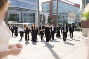 Wedding party walking confidently through a modern city setting with glass buildings in background.