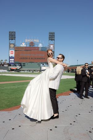A couple celebrates their wedding at Oracle Park baseball stadium with the scoreboard visible in background.