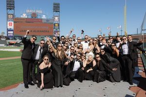 Large group of wedding guests posing for a panoramic photo at a baseball stadium.