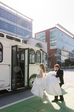A classic white trolley bus serves as backdrop for a wedding photo shoot in an urban setting.