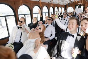 Wedding party celebrates in a trolley bus, everyone dressed in formal black and white attire.